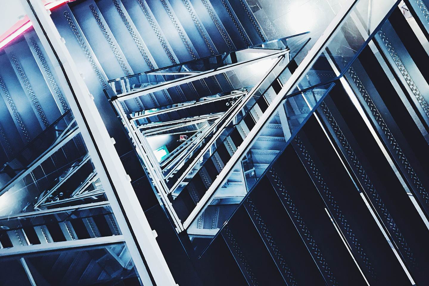 Abstract blue-toned view down a steel and glass stairwell forming nested triangles