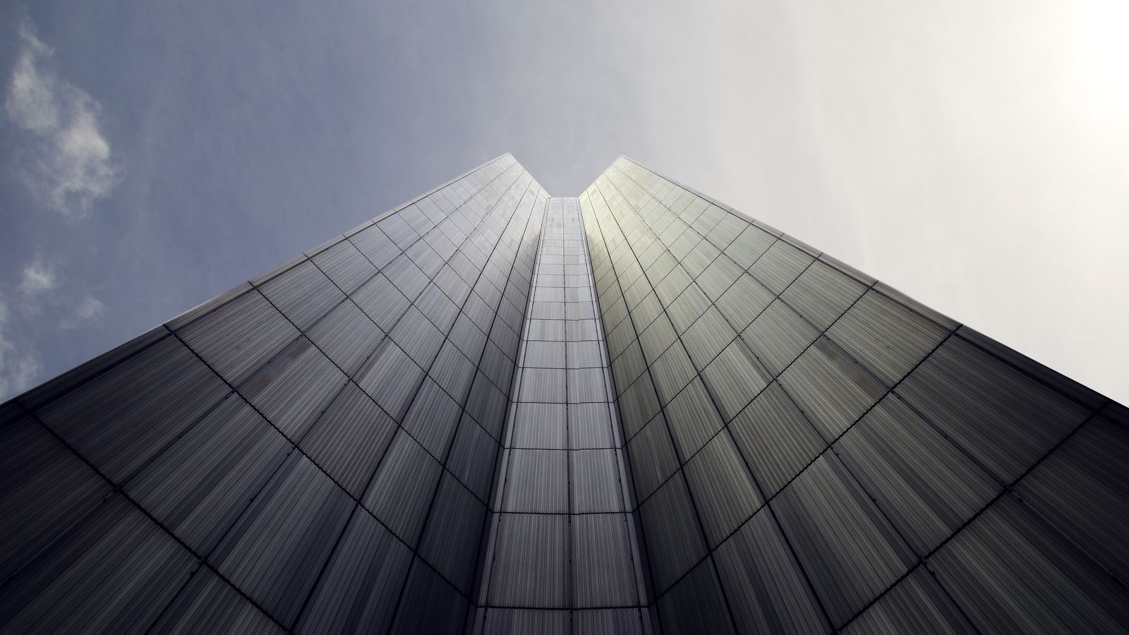 Monochrome upward view of a dark glass-panelled tower converging into a grey sky