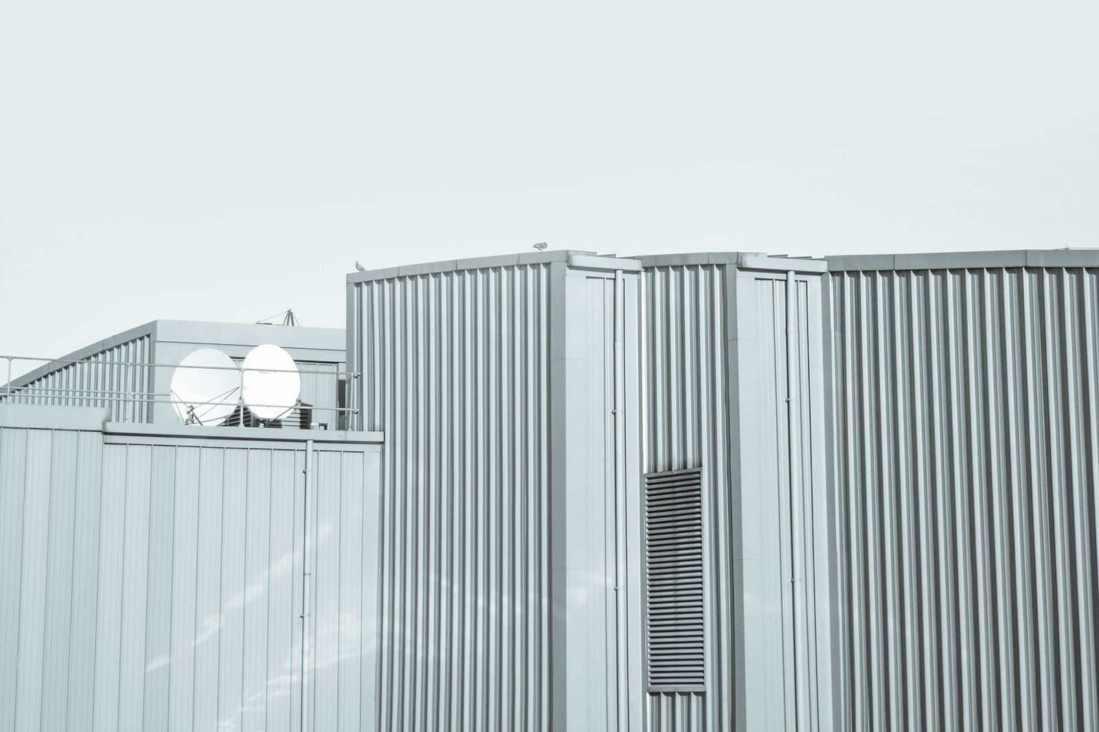 Minimal light-grey metal-clad industrial building with rooftop equipment beneath a pale overcast sky