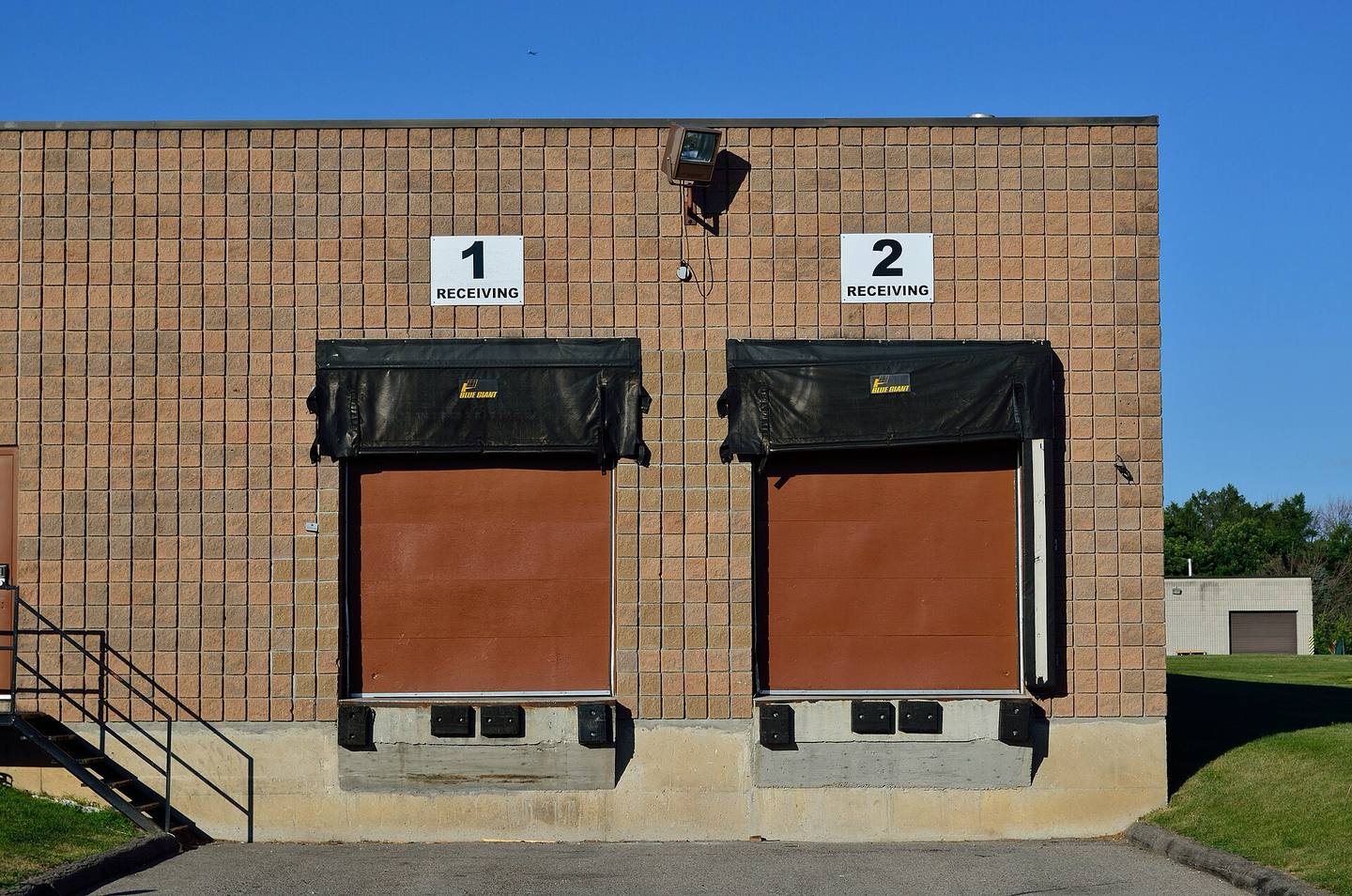 Two numbered loading dock doors with dock seals on a tan block warehouse wall under a clear blue sky