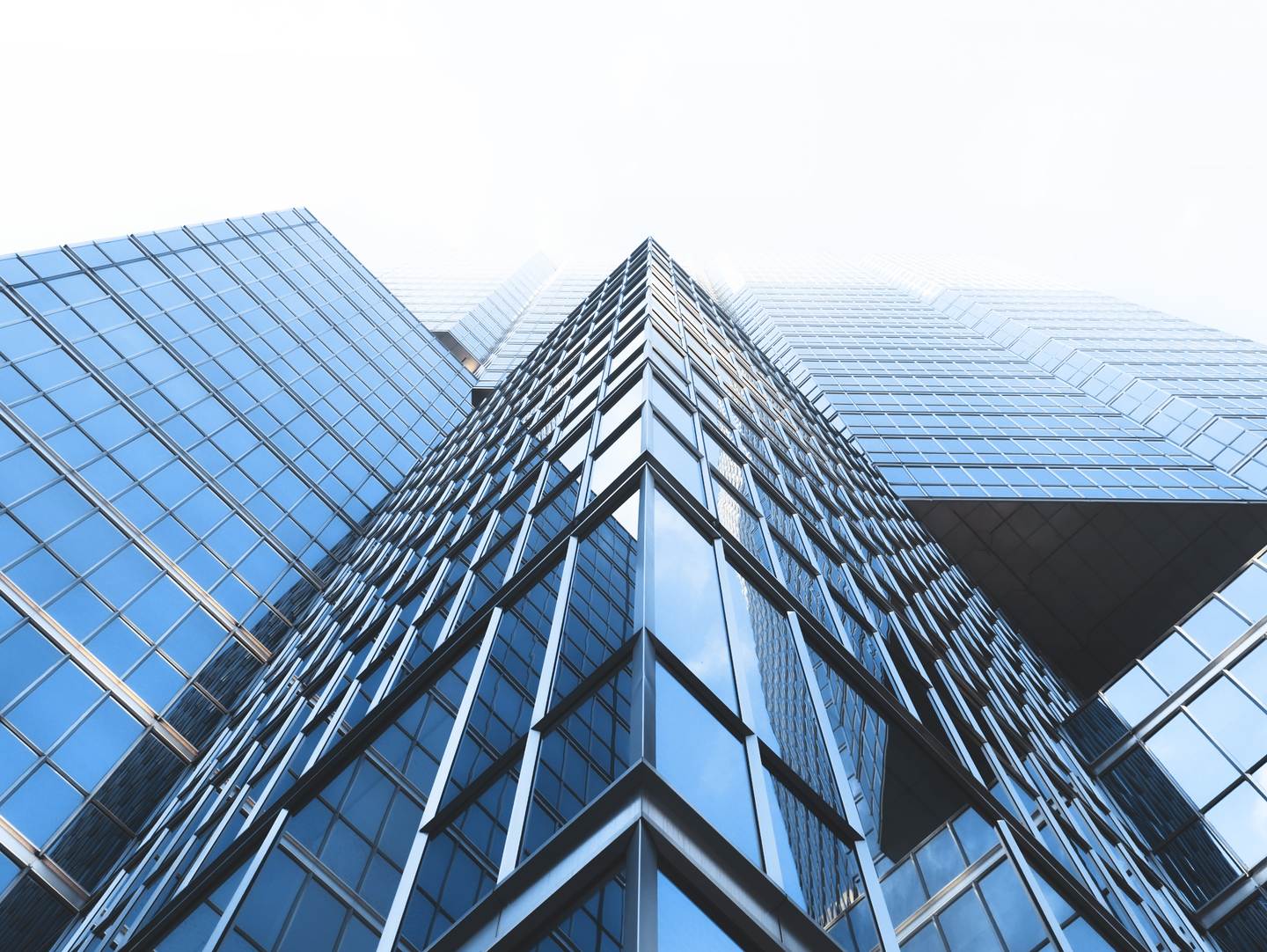 Low-angle view of a blue glass curtain-wall office tower rising into a pale, hazy sky