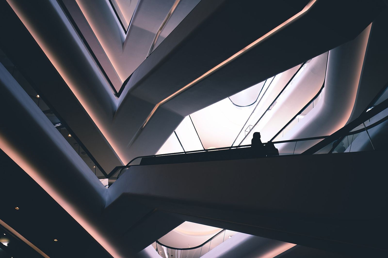 Dramatic low-light view up through the curving balconies and escalators of a multi-level shopping centre, with one silhouetted shopper